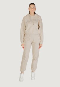 Set di felpa e pantaloni tuta beige con texture a costine, con logo argentato sul fronte. Vestibilità ampia con polsini ed orli elastici.