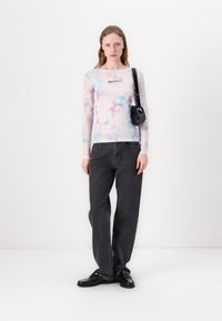 Dulga prozirna majica dugih rukava u pastelnom tie-dye uzorku s kvadratnim izrezom i logotipom, u kombinaciji s tamnim trapericama visokog struka i crnim cipelama.