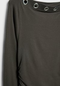 Mørkegrøn top med rynket sidesyning, der har metalliske grommetdetaljer langs udskæringen. Glat, strækbart stof.