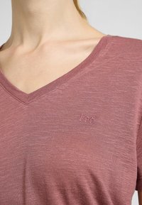 Maglietta a V leggera di colore rosa, realizzata in tessuto morbido, con una sottile trama e un logo ricamato "Lee" sull'area sinistra del petto.