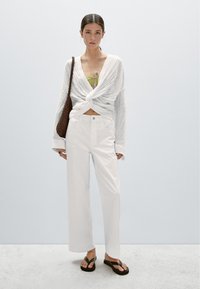 Vita löst sittande byxor i kombination med en texturerad, vriden vit topp och en grön linne. Accessoarer: en flätad brun väska och flip-flops.