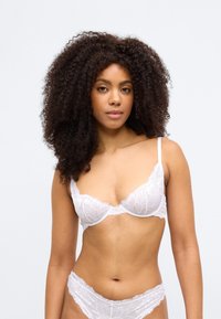 Balts mežģīņu krūšturis ar ziedu rakstu, ar stīpiņām atbalstam, regulējamām lencēm un atbilstošām mežģīņu biksītēm. Delikāta, viegla tekstūra.