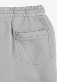 Jasnoszare spodnie dresowe z elastycznym pasem i jedną tylną kieszenią w kształcie prostokąta o gładkiej fakturze.