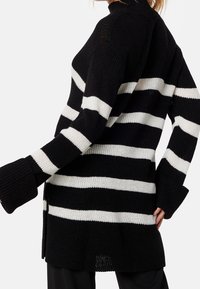 Strickjacke mit schwarzen und weißen horizontalen Streifen, langen Ärmeln und lockerem Sitz. Der Stoff hat eine strukturierte, grob gestrickte Optik.