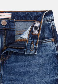 Jeans in denim con un lavaggio blu scuro, dotati di patta con zip, cuciture arancioni e etichetta con marchio vicino alla vita. Design dei taschini dettagliato.