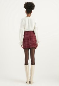 Top blanco de manga larga con cuello con volantes, combinado con una mini falda de cuadros rojos, medias negras y botas de tacón blancas hasta la rodilla.
