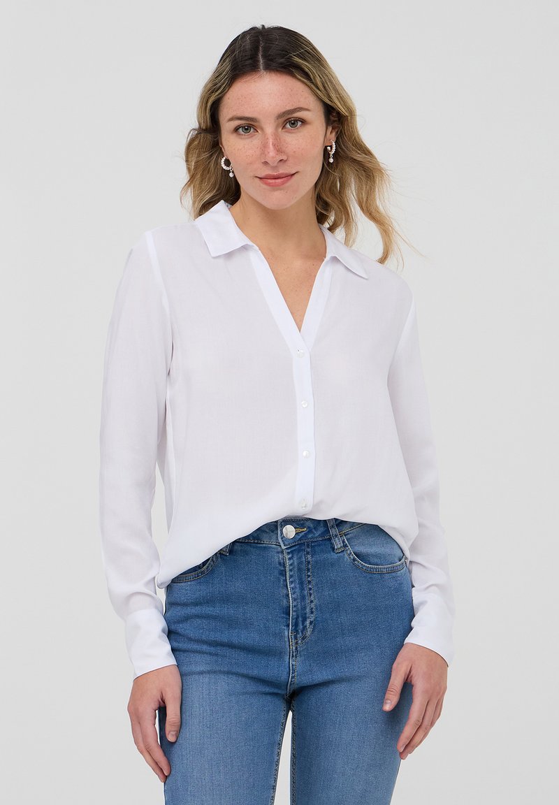 Camicia bianca a maniche lunghe con colletto, caratterizzata da una texture setosa e una vestibilità rilassata, abbinata a jeans in denim blu.