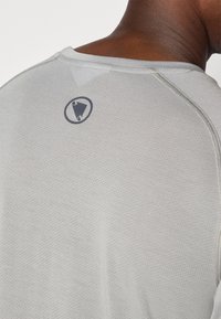 Light gray athletic shirt with a textured pattern, featuring a round logo on the back near the neckline. Seam details visible.