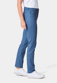 Hellblaue elastische Hosen mit glatter Textur, die seitliche Taschen und ein schlankes Design aufweisen. Kombiniert mit weißen Sportschuhen.