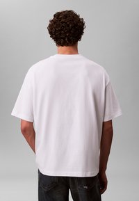 Hvit bomulls-T-skjorte med avslappet passform, korte ermer og rund hals, sett bakfra, kombinert med mørke denimjeans.