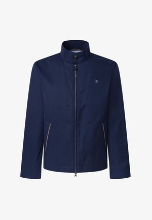 Chaqueta azul marino con cuello alto, cierre frontal y dos bolsillos laterales con acentos de color claro. Textura de tela suave y mate.