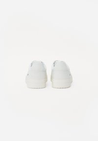Hvide sneakers med en glat læderoverdel og gummiklub, med minimalistisk design og et diskret logo på hælen.