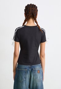 Cămașă neagră cu mâneci scurte, având dungi albe pe laterale și fundițe la mâneci, combinată cu blugi din denim deschis, ce au buzunare aplicate la spate.