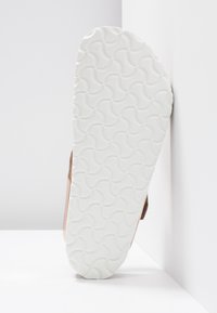 Sandala s glatkom smeđom gornjom površinom i fleksibilnom bijelom gumenom potplatom s valovitom šablonom. Potplat pokazuje znakove trošenja od korištenja.