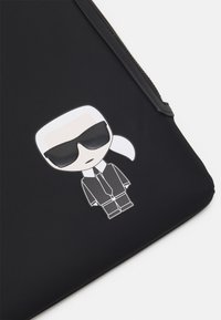 Housse d'ordinateur portable noire avec une texture lisse, présentant une figure de dessin animé en costume et lunettes de soleil imprimée sur le devant.