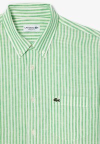 Camisa de botones a rayas verdes y blancas, de tela de algodón, corte regular, con un pequeño logotipo bordado en el bolsillo del pecho izquierdo.