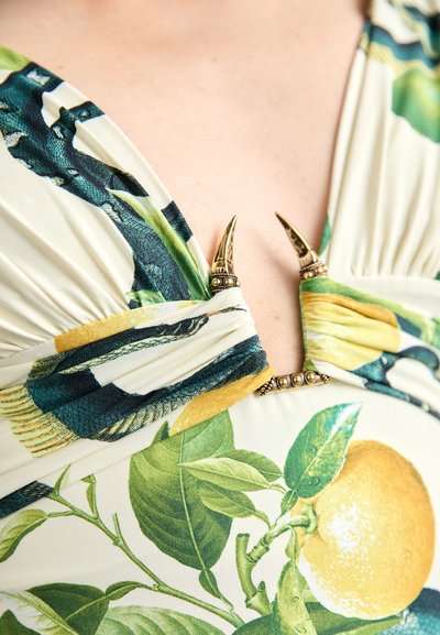 Īsās piedurknes kleita ar ziedu rakstu, kurā redzami zaļi lapas un dzelteni citroni. Centrālā detaļa ietver metāla naglu akcentus.