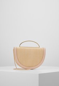 Torebka w kształcie półksiężyca, pleciona w kolorze beżowym z jasnoróżowymi wykończeniami, złotą rączką oraz złotym łańcuszkiem na białym piedestale.