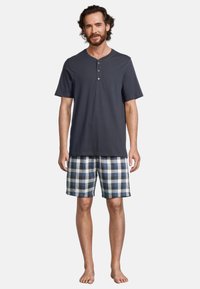 Maglietta henley grigio scuro a maniche corte con tre bottoni, abbinata a pantaloni corti a quadri blu e bianchi. Vestibilità comoda, adatta per il relax.