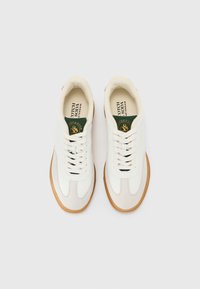 White sneakers with a smooth leather and suede upper, rubber sole, round toe, and contrasting green and gold logo on a padded tongue.
