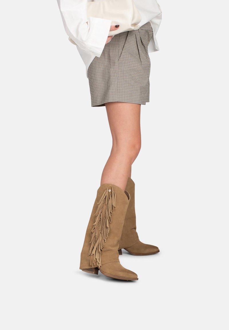 Bruine suède kniehoge laarzen met franjes, een spits toelopende neus en een gestapelde hak, gecombineerd met een geruit korte broek outfit.