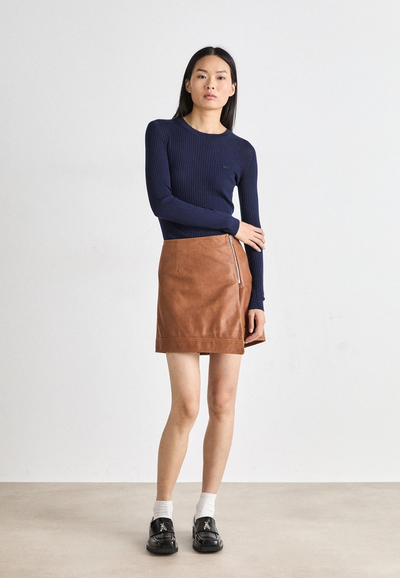 Navy ribbed langemouwen top gecombineerd met een bruin leren minirok met een zijrits. Model draagt zwarte schoenen met witte sokken.