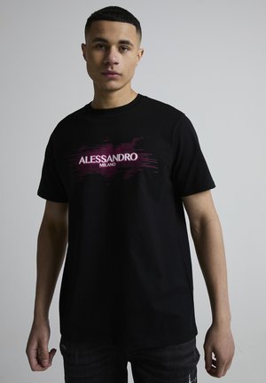 Ung mand med kort hår iført en sort T-shirt med rød og hvid "ALESSANDRO MILANO" tekst foran, stående mod en ensfarvet grå baggrund.