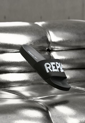 Musta liukusandaali, jossa valkoinen "REPLAY"-teksti, valmistettu sileästä synteettisestä materiaalista, leveällä remmillä ja avoimella varvasosalla.