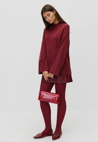 Bordowy, oversize'owy sweter z dzianiny z prążkowanymi mankietami, dopasowana skórzana mini spódnica, bordowe rajstopy, błyszcząca torebka oraz czółenka na spiczastym obcasie.