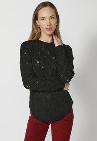 Czarny sweter robiony na drutach z fakturowanym wzorem, z długimi rękawami i okrągłym dołem. Tkanina ma subtelny połysk i otwarty splot.