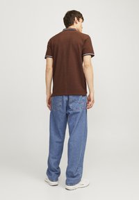 Bruine polo met witte kraag en accent op de mouwen, gecombineerd met loszittende blauwe spijkerbroeken en witte sneakers.