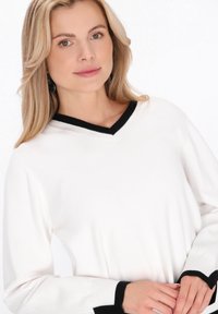 Pulover alb cu decolteu în V negru și accente negre la manșete. Confecționat dintr-un material moale, cu un croi lejer.