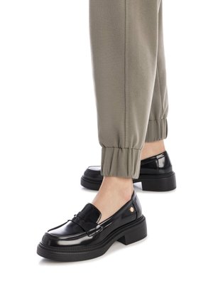 Mocassini neri in pelle verniciata con suola spessa e dettagli laterali, abbinati a pantaloni elasticizzati olive verdi con i polsini.