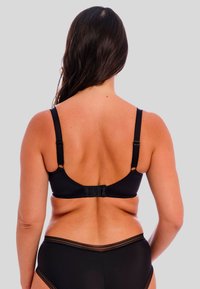 Black bra with adjustable straps and hook closure. Smooth material, semi-sheer accents, and a rounded back design. Panty not included.