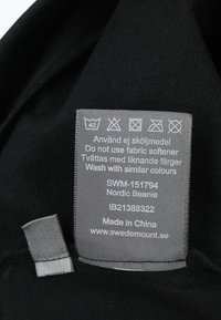 Beanie di tessuto nero con un'etichetta di cura grigia. L'etichetta include istruzioni per il lavaggio e dettagli sul prodotto. Texture morbida, design semplice.