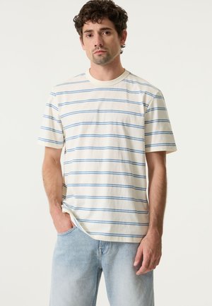 Kurzärmeliges T-Shirt mit Rundhalsausschnitt aus cremeweißem Baumwollstoff mit blauen horizontalen Streifen. Legerer Schnitt mit entspannter Silhouette. Jeans aus Denim.