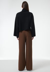 Pull noir court avec un col haut et des manches larges, associé à un pantalon marron taille haute, ample, avec des détails sur les poches arrière.