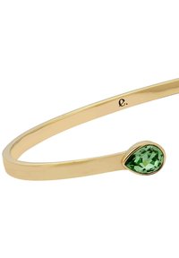 Goldfarbener Armreif mit glattem, geschwungenem Design und einem tropfenförmigen grünen Edelsteinakzent. Minimalistischer Stil mit polierter Oberflächenstruktur.