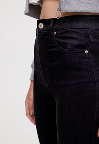 Jean en denim noir à taille haute, avec une poche avant, des garnitures métalliques brillantes et une texture subtile.