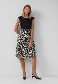 Haut noir ajusté avec des manches courtes, jupe fluide en imprimé léopard beige et noir, portée avec des talons slingback noirs.
