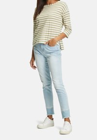 Randig olivgrön och krämfärgad topp med trekvartslånga ärmar, kombinerad med ljusblå slitna jeans och vita sneakers.