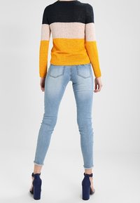 Strickpullover in Schwarz, Pink, Orange und Gelb gestreift; kombiniert mit hellblauen Skinny-Jeans und dunkelblauen Riemchensandalen.