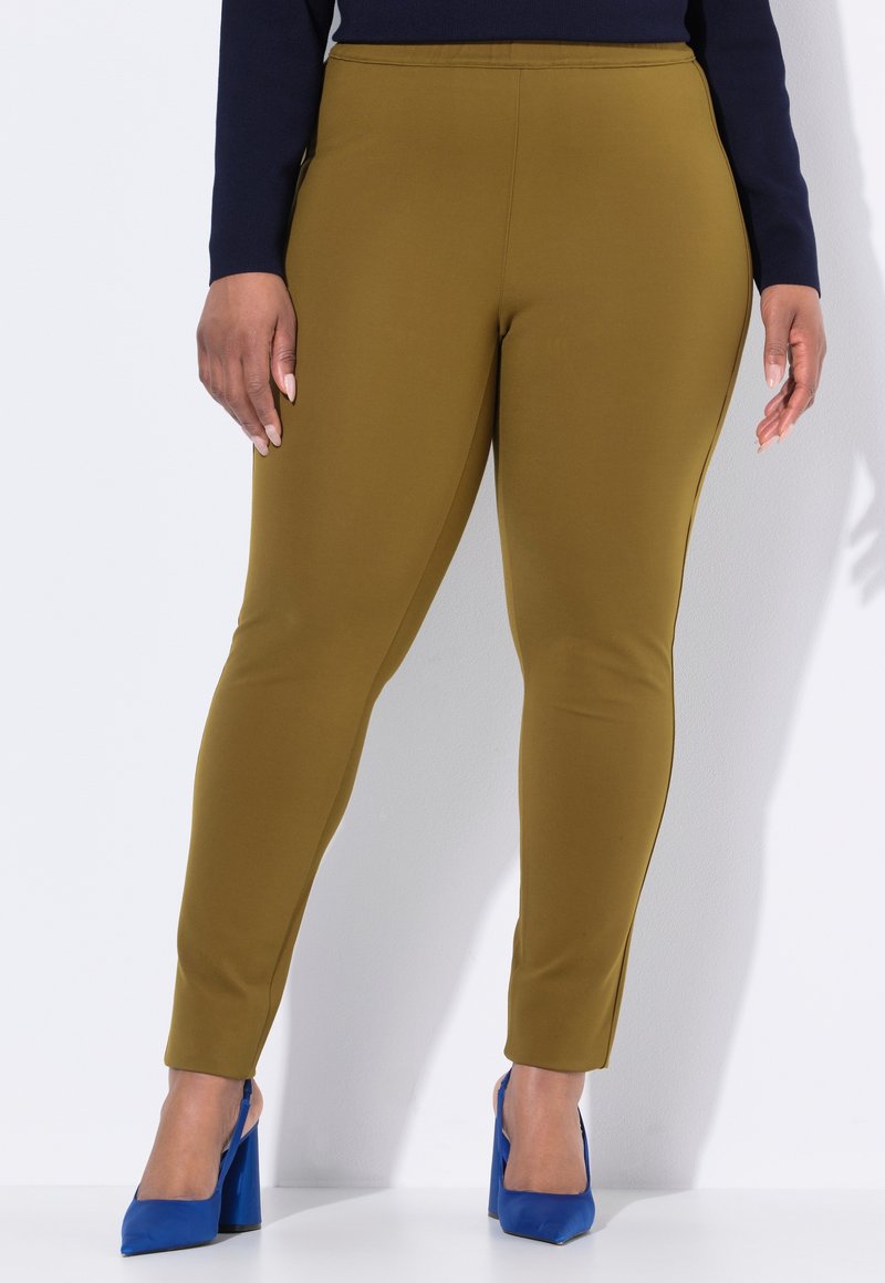 Olivgröna leggings i elastisk tyg, med slim fit och ankellång klippning, tillsammans med blå högklackade skor.