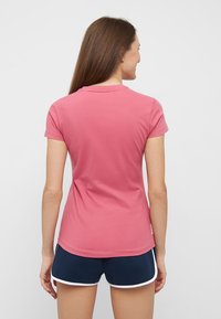 T-shirt rose à manches courtes avec une texture douce et un col arrondi, associée à un short bleu marine avec une bordure blanche.