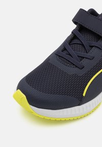 Scarpa sportiva con tomaia in rete di un blu navy scuro e accenti gialli. Progettata con una suola ammortizzata e una fascia regolabile per una vestibilità sicura.