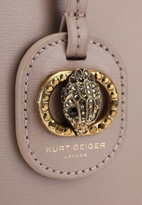 Jasnobeżowa torebka z wyraźnymi złotymi detalami metalowymi, posiadająca teksturowany wzór i czarne akcenty z kamieni szlachetnych. Wyświetlona nazwa marki.