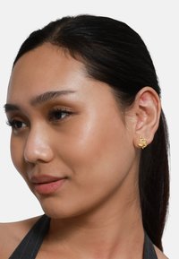 Orecchini a forma di serpente d'oro esposti sull'orecchio di un modello. Il design presenta curve morbide e una finitura lucida, aggiungendo un tocco moderno.
