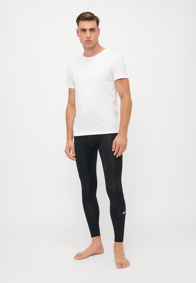 Fehér, rövid ujjú póló fekete szorító leggingsszel párosítva, amelyen a lábszáron egy kis fehér Nike logo található.