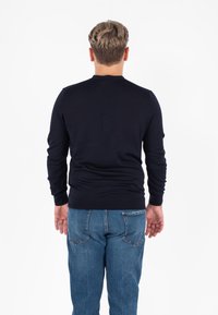 Maglione lavorato a maglia blu navy con collo tondo e maniche lunghe, abbinato a jeans di denim blu chiaro. Il maglione ha un design aderente e una texture liscia.