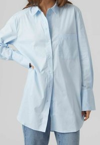 Camicia azzurra oversize con chiusura a bottoni, maniche lunghe e un'unica tasca sul petto. Realizzata in tessuto morbido con colletto classico.